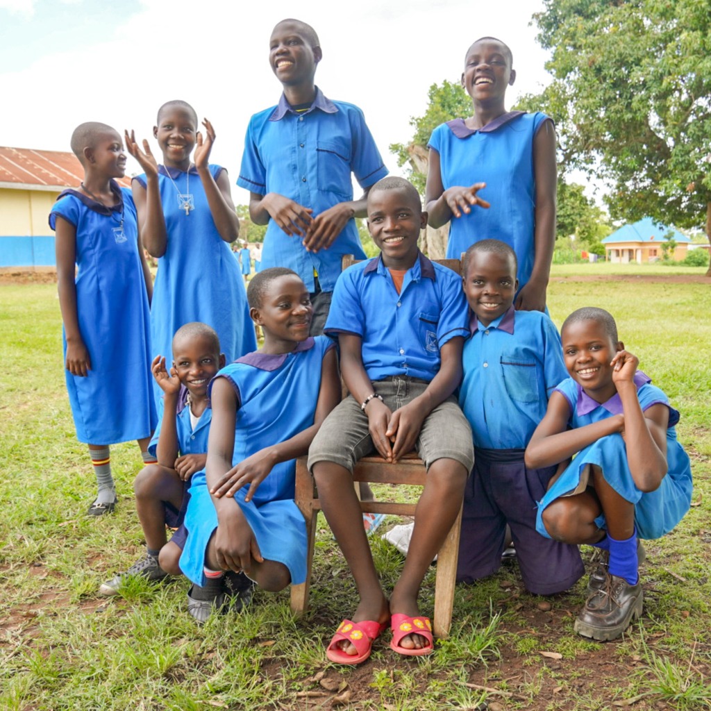 Group of smiling Ugandan students in blue school uniforms posing together outside