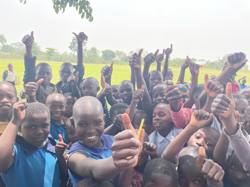School children in Uganda smiling and giving a thumbs-up to the camera