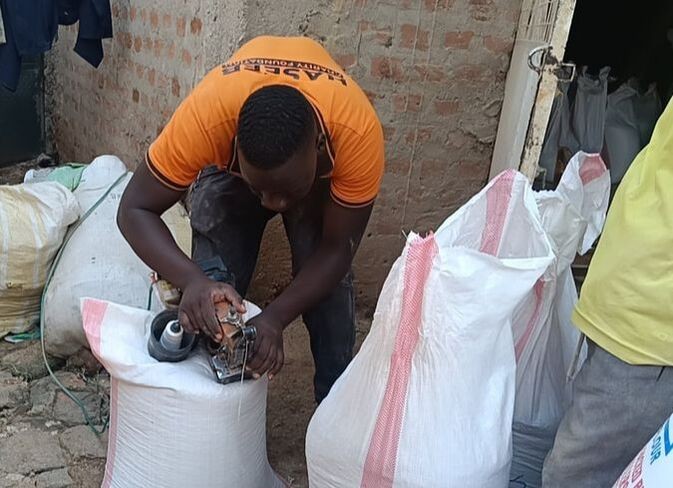 A GVC partner using a handheld industrial sewing machine to securely seal the bags of emergency food before distribution