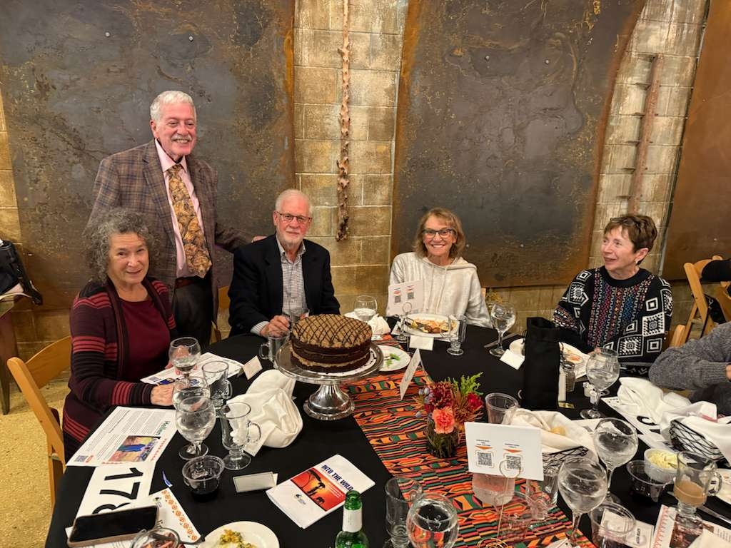 Gala guests smiling around their dining table, featuring a beautiful custom chocolate cake