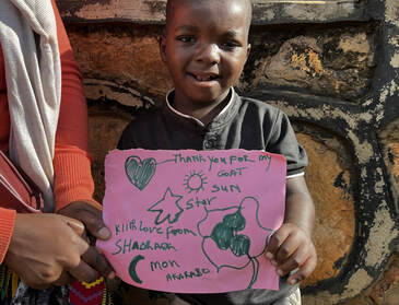 A young child holding a handmade thank you note that says 'Thank you for my goat'